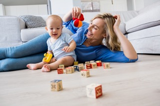 Mother looking at baby boy playing with toys in living room
